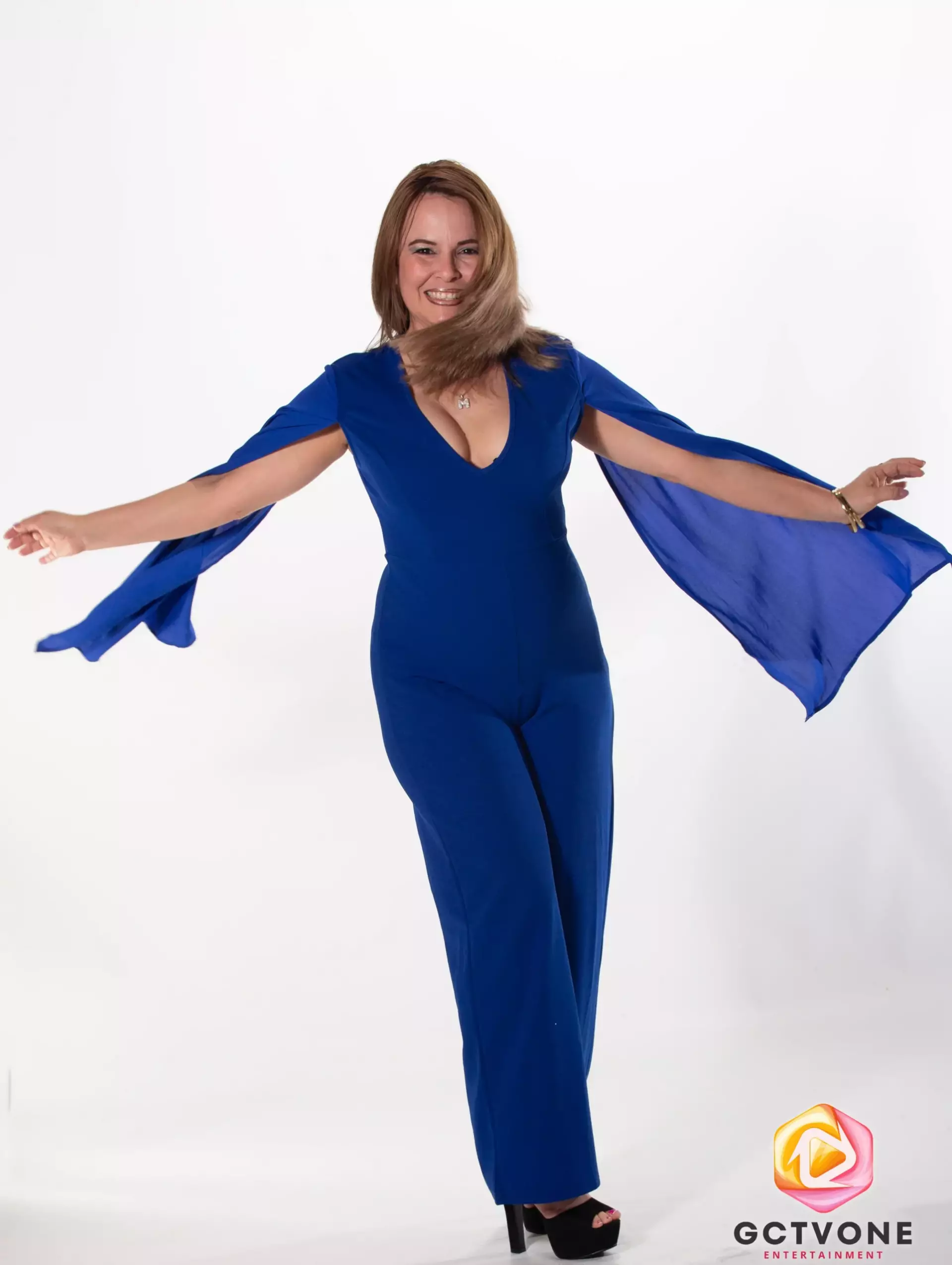 Donde la alegría se encuentra con la música. Marelis en sesión de fotos con un traje azul, sonriente y en movimiento con los brazos abiertos, transmitiendo alegría y libertad.